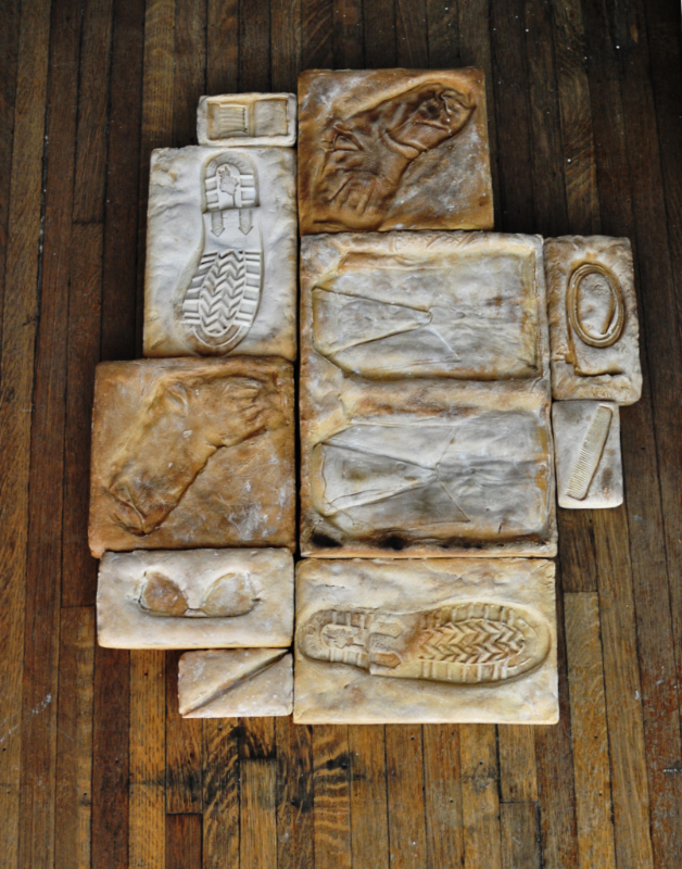 blocks of baked salt dough with imprints of shoeprints, belts, socks, sunglasses, comb, dress shirt, etc...